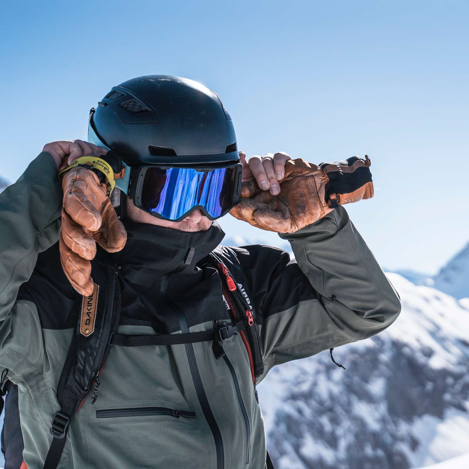 Homme portant un casque de ski et des lunettes de protection avec les montagnes derrière lui