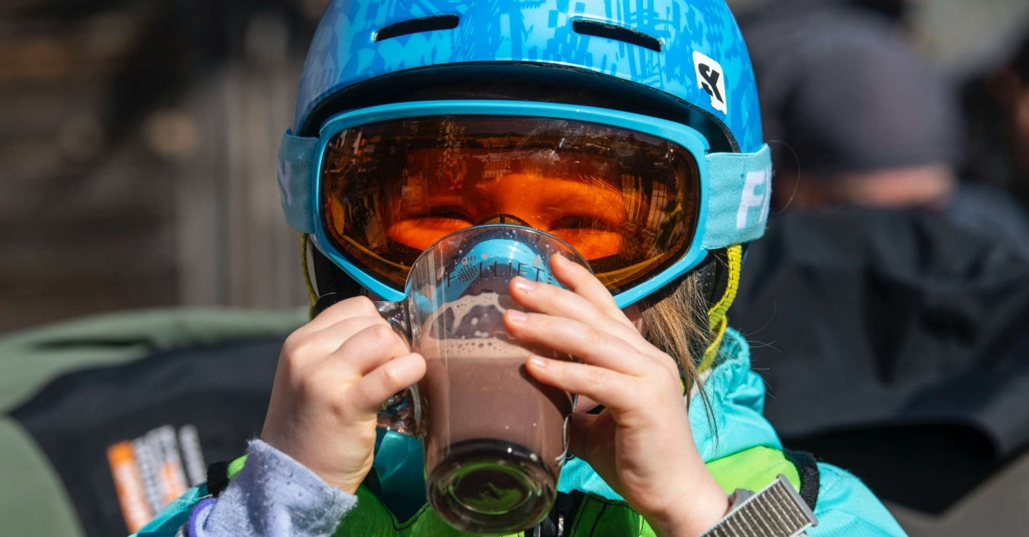 Child enjoying hot chocolate whilst skiing scaled e1660639717163